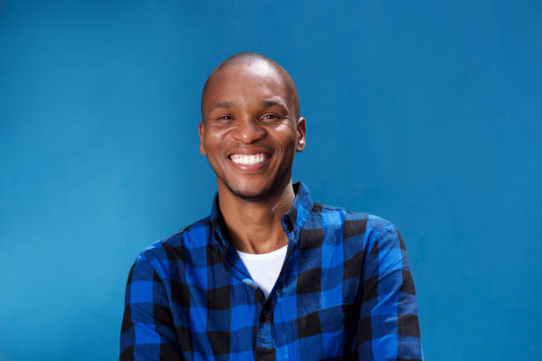 smiling young african man smiling against blue wall Close up portrait of smiling young african man standing with his arms crossed against blue background men hairstyle afro cool stock pictures, royalty-free photos & images