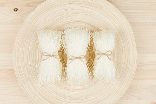 Sheaf raw asian cellophane noodles on plate on beige wooden board , top view.