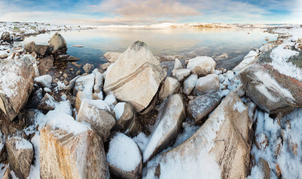 Panoramic view of norwegian lake at sunset, rocks covered with snow on foreground
