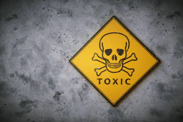 A square yelow sign with the international symbol for poison and other chemical / biological hazard. The sign is set on a dirty concrete wall surface.