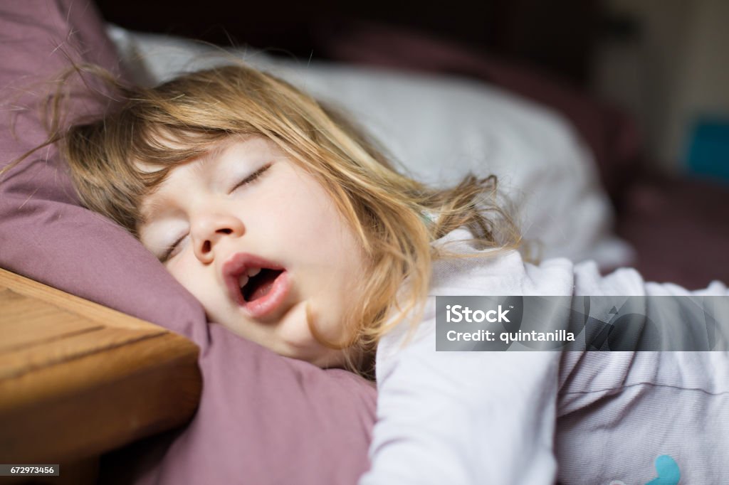 funny face of child sleeping on king bed funny face expression with open mouth of blonde caucasian three years old child,  sleeping on  king bed Child Stock Photo