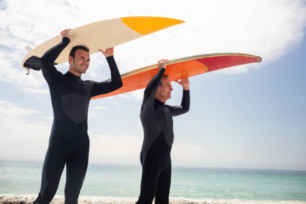 istock Happy father and son carrying a surfboard over their head 673007490