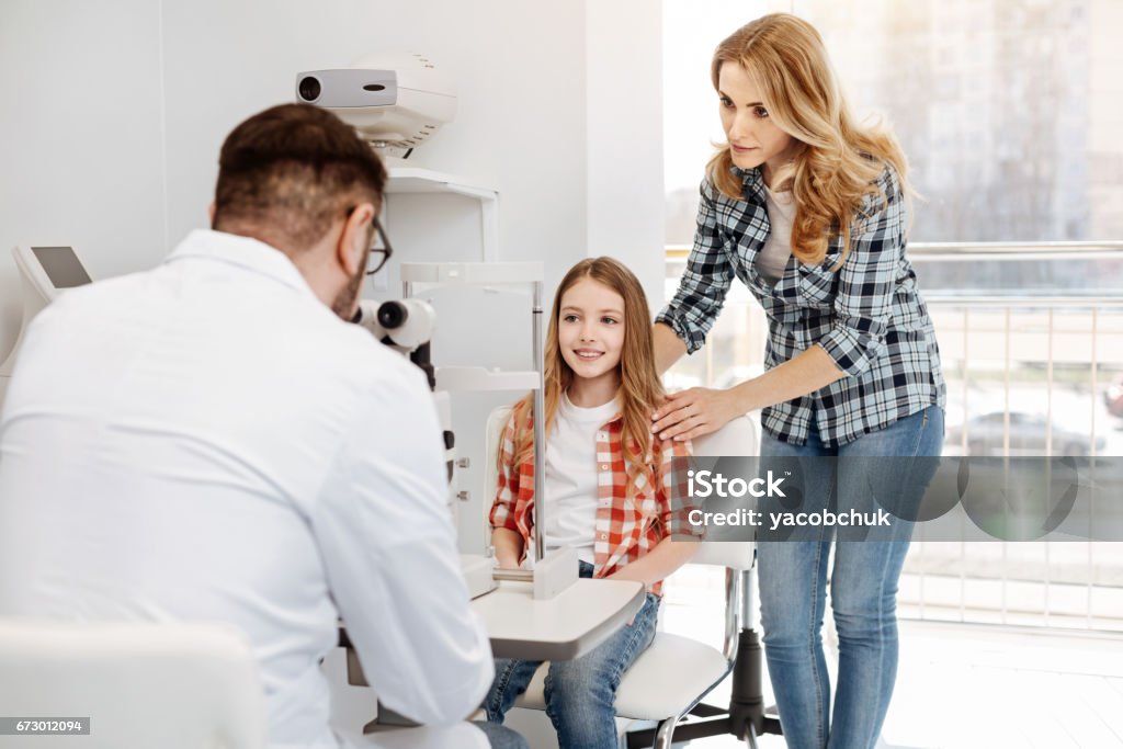 Young admirable teenager receiving doctors advice Family support. Loving mom and her pretty daughter sitting at ophthalmologists office and waiting for his verdict while he studying results of girls tests Helicopter Stock Photo