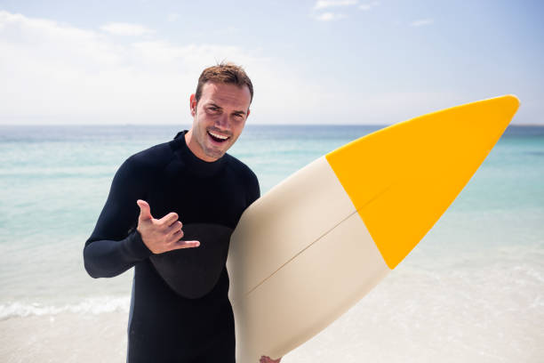 Portrait of surfer with surfboard gesturing hand sign on beach on a sunny day