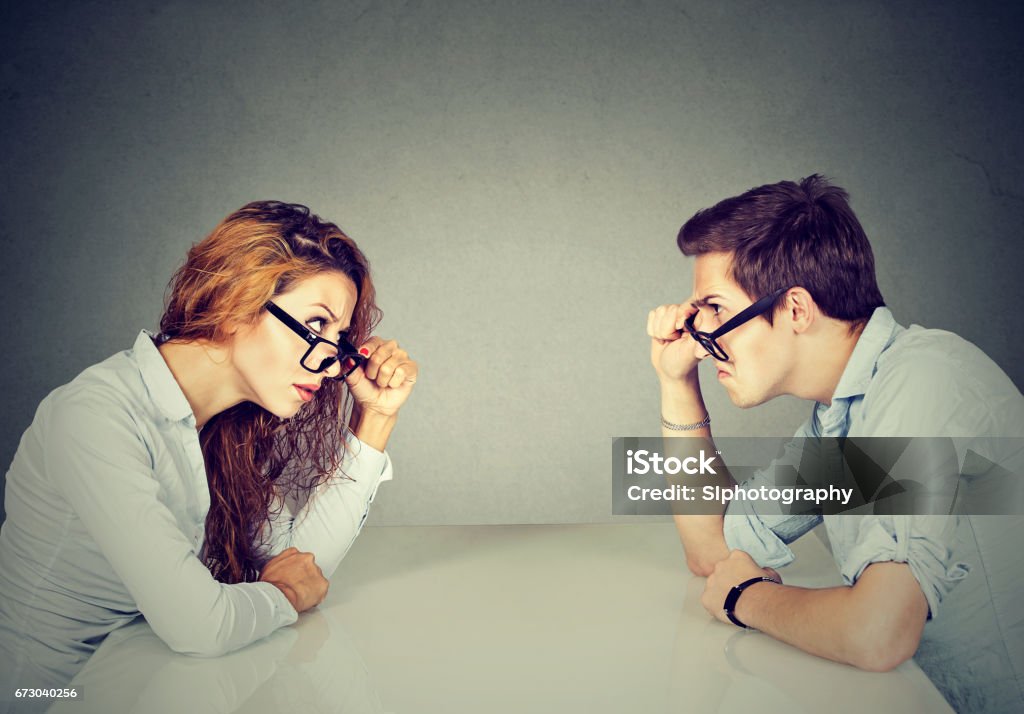 Angry man and woman sitting at table looking at each other with hatred and disgust Human Gender Stock Photo