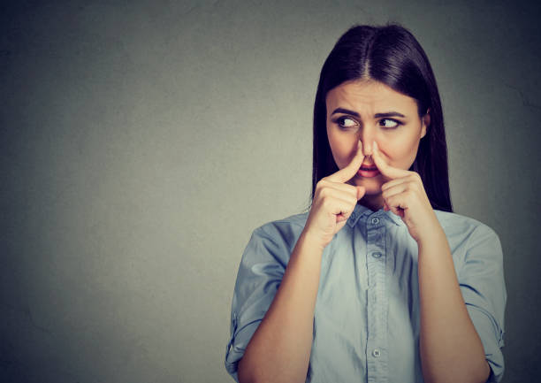 Woman pinches nose with fingers looks with disgust away something stinks bad smell stock photo