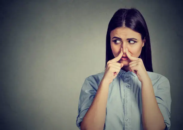 Photo of Woman pinches nose with fingers looks with disgust away something stinks bad smell