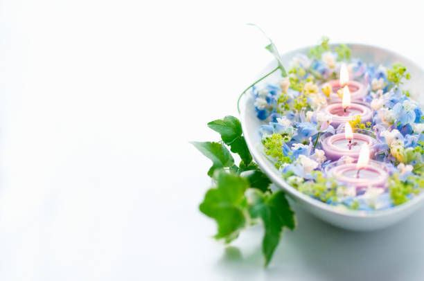 Two white candles with dried flowers and a fluffy white towel in the background.