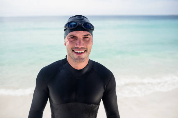 istock Young man in wetsuit and swimming goggles standing on beach 673046272