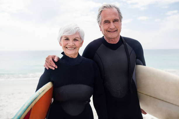 istock Senior couple in wetsuit holding surfboard on beach 673051482