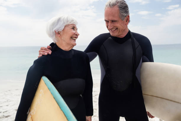 istock Senior couple in wetsuit holding surfboard on beach 673051570
