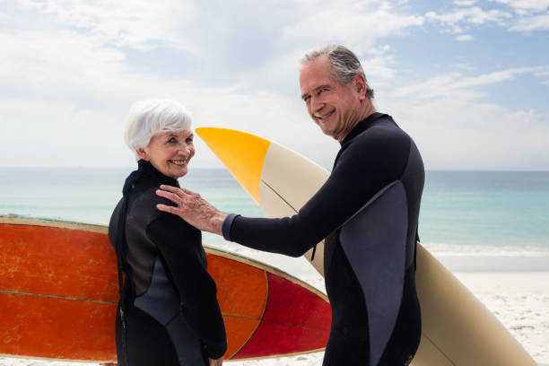 istock Senior couple in wetsuit holding surfboard on beach 673051878