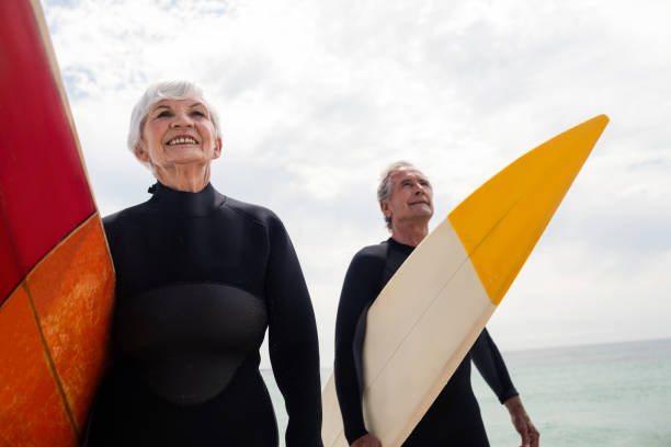 istock Senior couple in wetsuit holding surfboard on beach 673052360