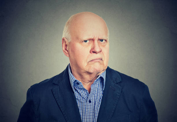 Portrait of an angry, grumpy senior business man, isolated on gray background Portrait of an angry, grumpy senior business man, isolated on gray background sulking stock pictures, royalty-free photos & images
