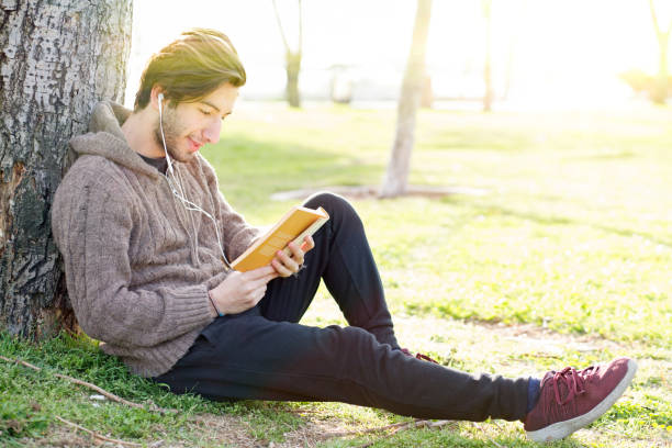 istock Young man reading book in the park 673084016