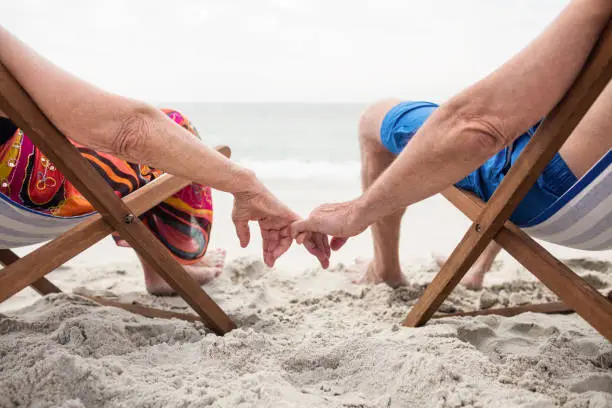 Rear view of senior couple sitting on deckchairs and holding hands while relaxing on the beach