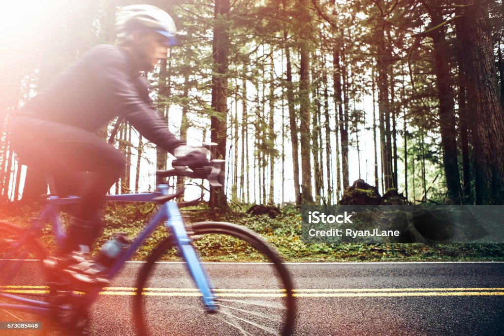 Cyclist Riding Mountain Road on Racing Bike A man cycling in a beautiful Oregon state forest setting on the road to Larch Mountain. He has a bright blue street bike that stands out from the green of the surrounding trees. Profile view, with blurred motion as he speeds past the stationary camera. Road Cycling Stock Photo