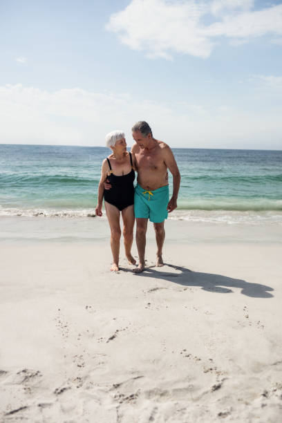 istock Happy senior couple embracing while walking on beach 673090910