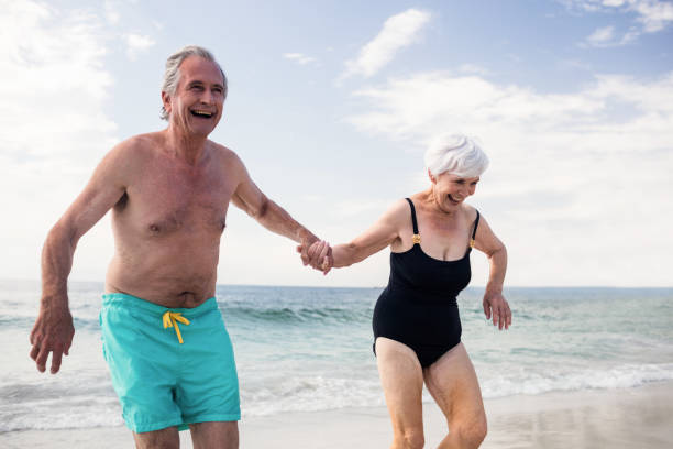 istock Happy senior couple holding hands and running on the beach 673096476