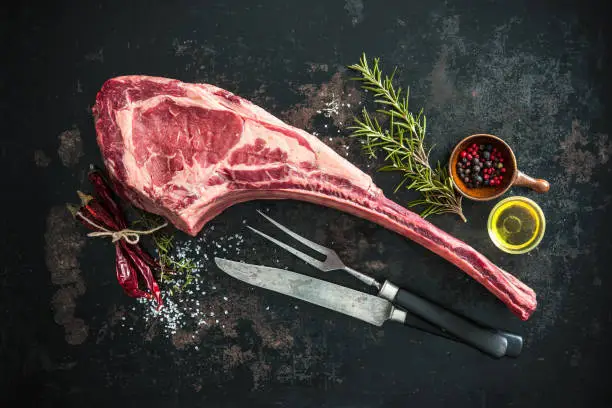 Dry aged raw tomahawk beef steak with ingredients for grilling: