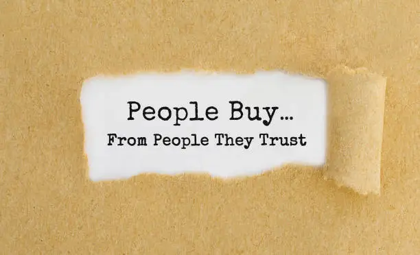 Photo of Text People Buy From People They Trust appearing behind ripped brown paper.