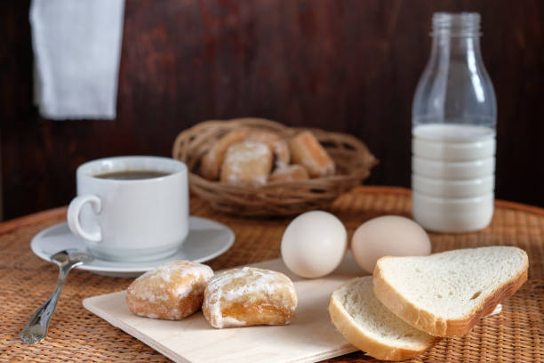 Breakfast with cup of coffee gingerbread eggs bread and milk in bottle on table soft lighted on dark background textured with scratches and with soft strip light near towel from sun