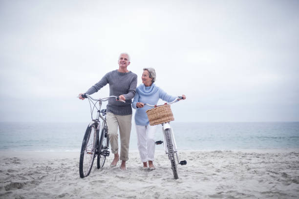 Senior couple having ride with their bike Senior couple having ride with their bike on the beach man 60s bicycle stock pictures, royalty-free photos & images