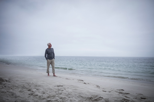 Thoughtful retired man standing on the beach on holidays