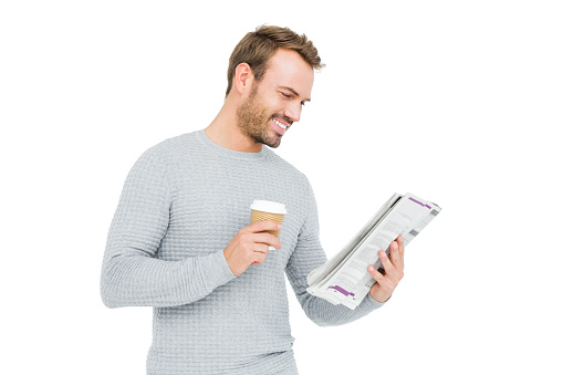 Young man holding disposable cup and reading newspaper on white background