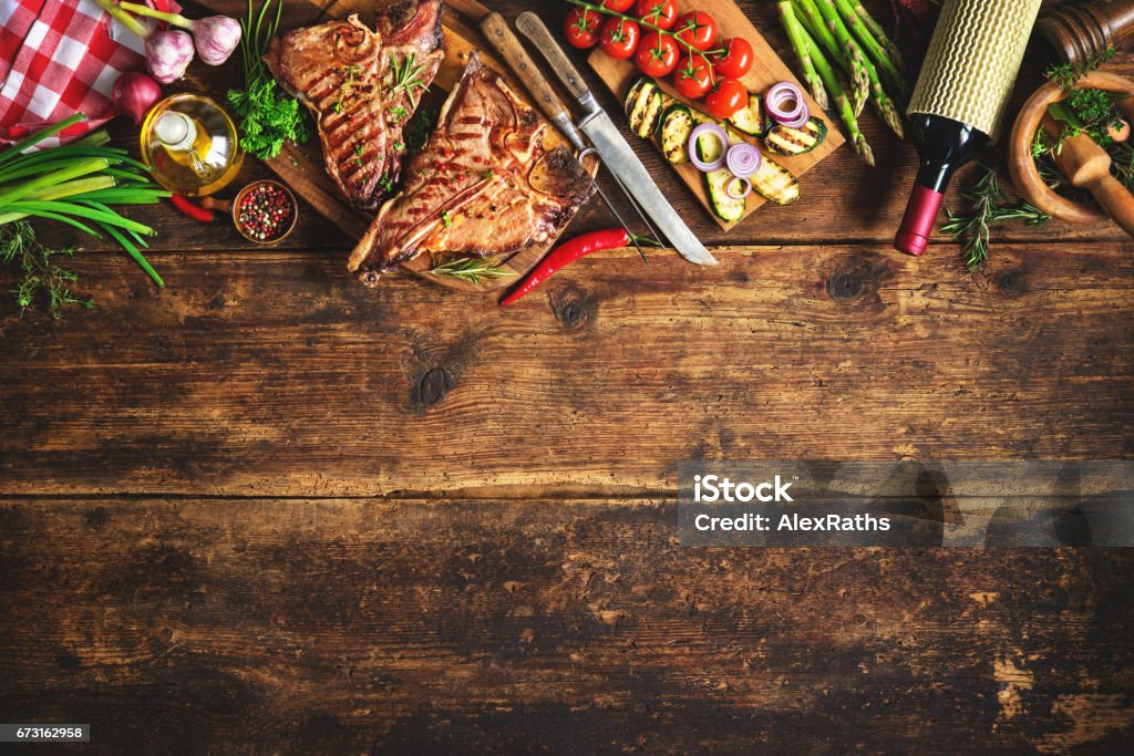 Grilled T-bone steaks with fresh herbs, vegetables ans wine bottle Grilled T-bone steaks with fresh herbs, vegetables and wine bottle on rustic wooden board Barbecue - Meal Stock Photo