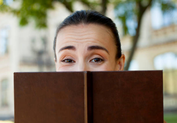 istock The girl looks out from behind a book. 673173322