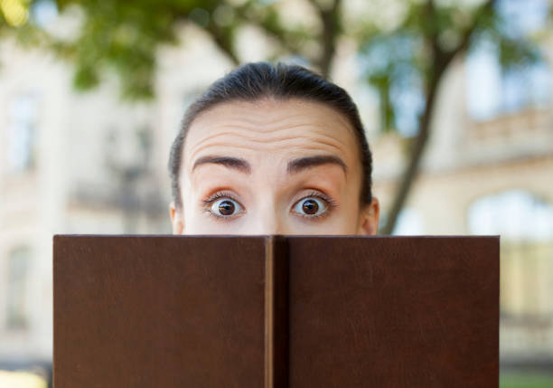 istock The girl looks out from behind a book. 673173360