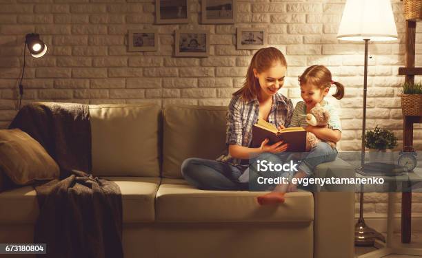 Foto de Família Antes De Ir Para A Mãe De Cama Lê Ao Seu Livro De Filha De Criança Perto De Uma Lâmpada À Noite e mais fotos de stock de Família