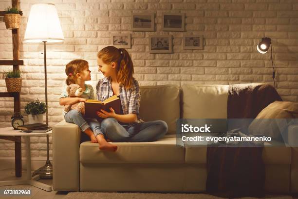 Family Before Going To Bed Mother Reads To Her Child Daughter Book Near A Lamp In The Evening-foton och fler bilder på Ljusutrustning