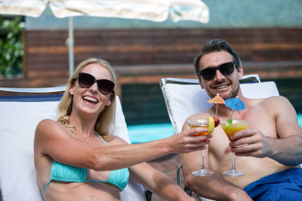istock Couple sitting on sun lounger toasting cocktail 673223754