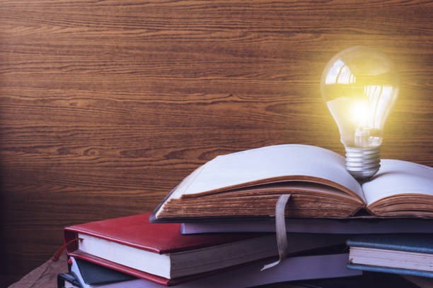 istock Open book with light bulb and hardback books on wood wall background. Free space for text. Selective focus 673263430