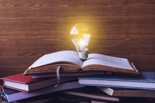 istock Open book with light bulb and hardback books on wood wall background. Selective focus 673263432