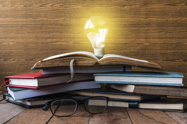 istock Open book with light bulb, hardback books and glasses on wooden table. 673263440