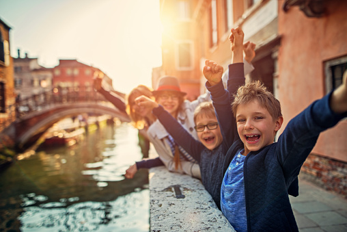 Mother and kids tourists visiting Venice, Italy. Family is cheering next to one of Venice canals.\n\n