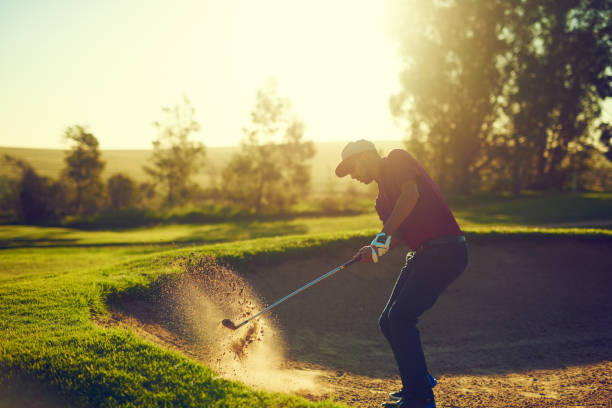 Every game comes with it’s challenges Shot of a young man hitting the ball out of the bunker during a round of golf game swing stock pictures, royalty-free photos & images
