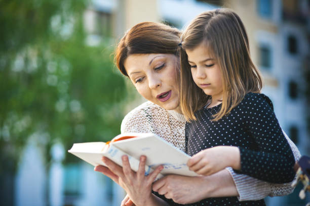 istock Mother with daughter reading book outdoor 673307664