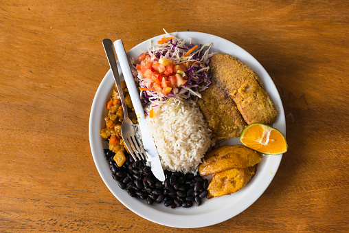 Directly above shoot of central american national dish on plate - scrambled egg, rice with beans, chilly and tomato, fried banana on the table.