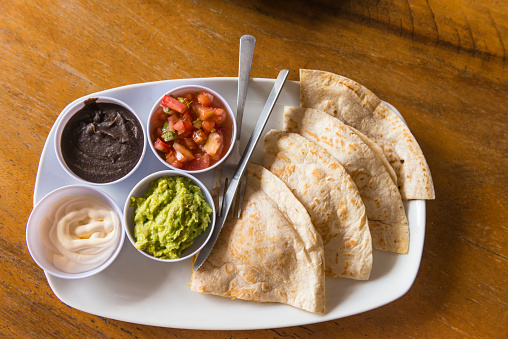 Directly above shoot of central american national dish on plate - chili with tomato, avocado, black bean and cream with slices of flet bread.