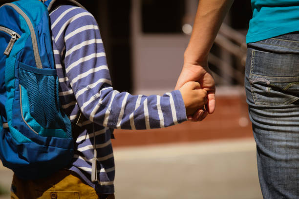 going to school- mother holding hand of son stock photo