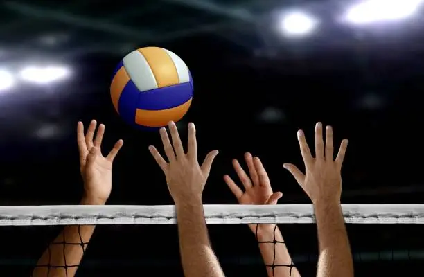 hand blocking volleyball spike over the net inside of a stadium