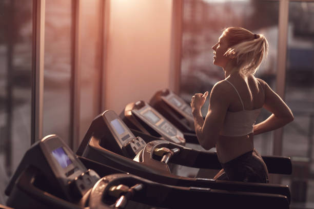 Young woman jogging on a treadmill in a gym. Athletic woman running on treadmill while having a sports training in a gym. sportsman professional sport side view horizontal stock pictures, royalty-free photos & images