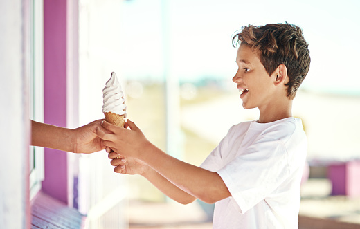 Shot of a happy young boy getting an ice-cream cone from a shop by the beach