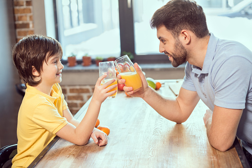 Side view of happy father and son drinking fresh juice together