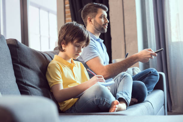 istock father watching movie and eating breakfast while son doing homework 673376054