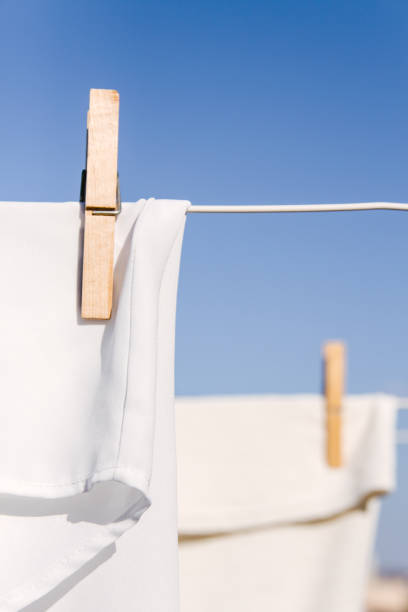 White clothes hung out to dry on a washing line in the bright warm sun. Background is a clear blue sky. stock photo